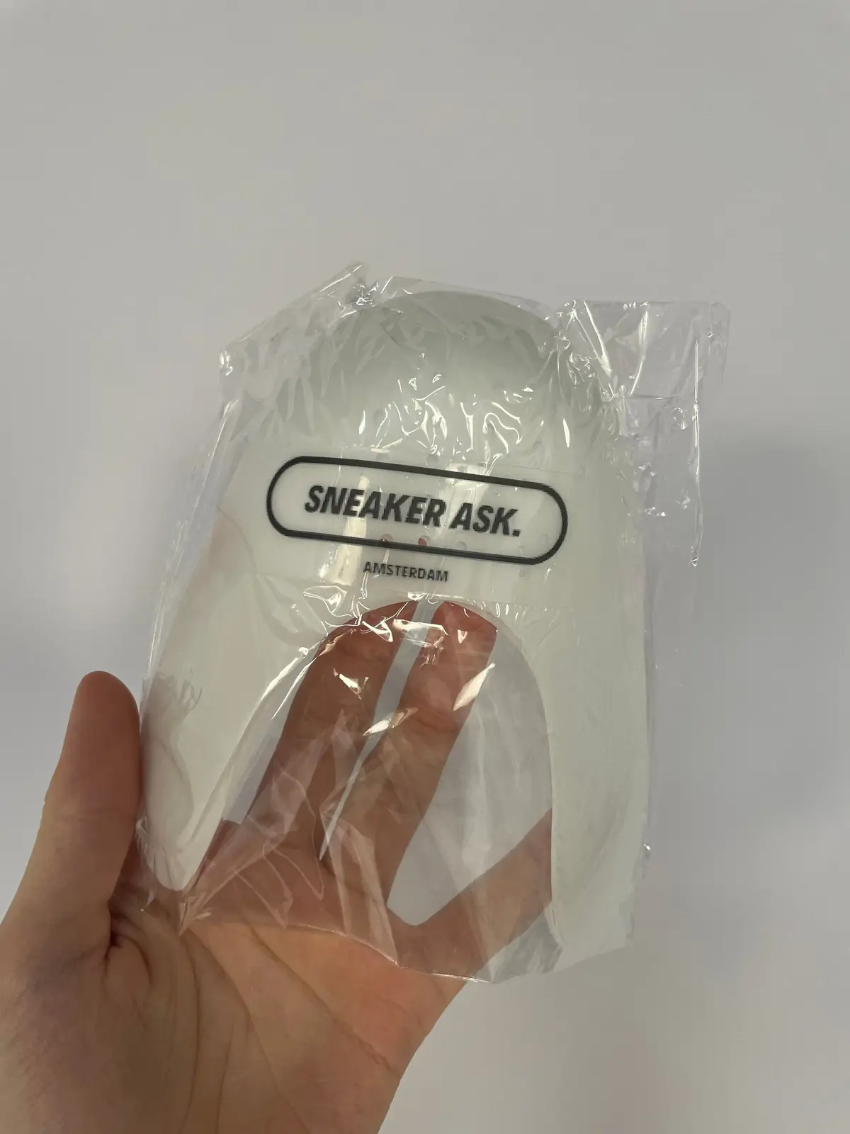 Hand holding a clear cushioning Anti-crease Plastic Shields with SneakerOne branding visible through the transparent packaging against a plain background.