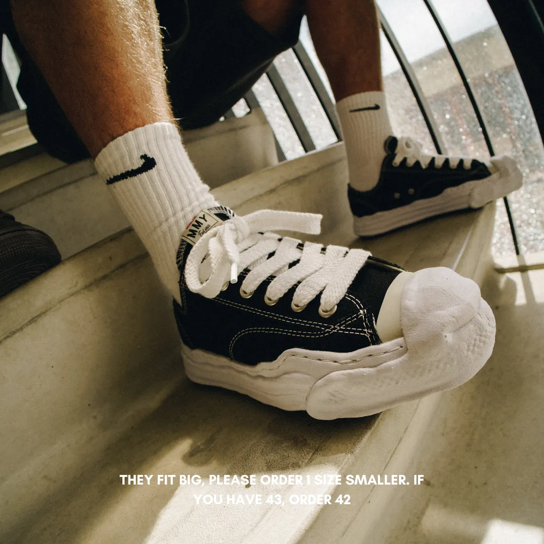 Close-up of person wearing Maison Mihara Yasuhiro Hank OG Sole Canvas Low Black sneakers paired with white Nike socks, showcasing exclusive Europe sneaker style with thick white laces and distinctive sole design. The real deal.