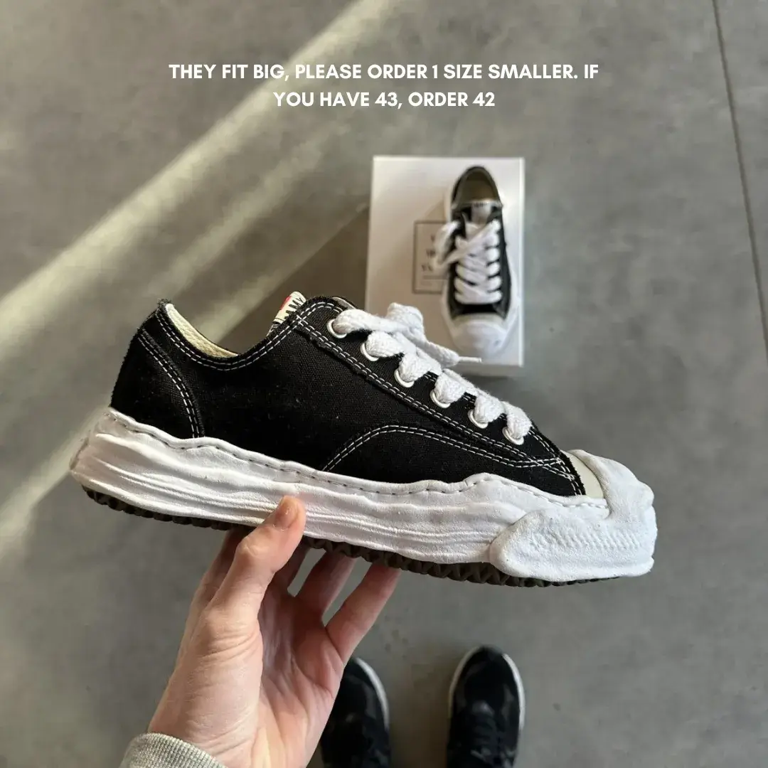 Hand holding a black and white Maison Mihara Yasuhiro Hank OG Sole Canvas Low Black sneaker with a unique, distorted sole design and white laces, exclusive in whole Europe.